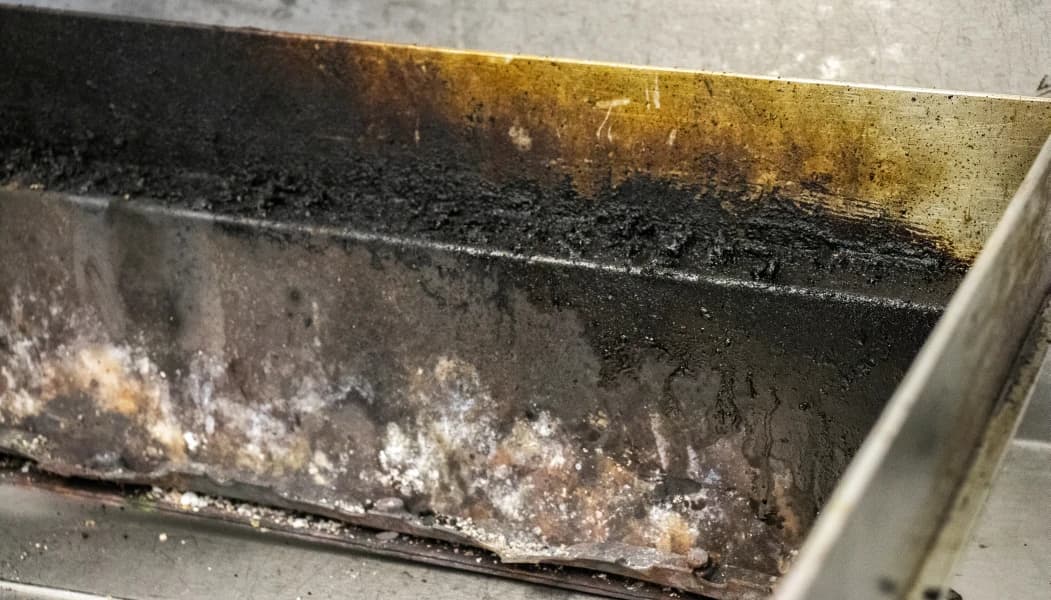 Close-up of grease, FOG, and dirt build-up in commercial kitchen equipment before professional cleaning by Bright.