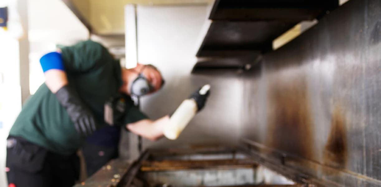 Bright technician spray cleaning commercial kitchen surfaces as part of professional hygiene and sanitation service.