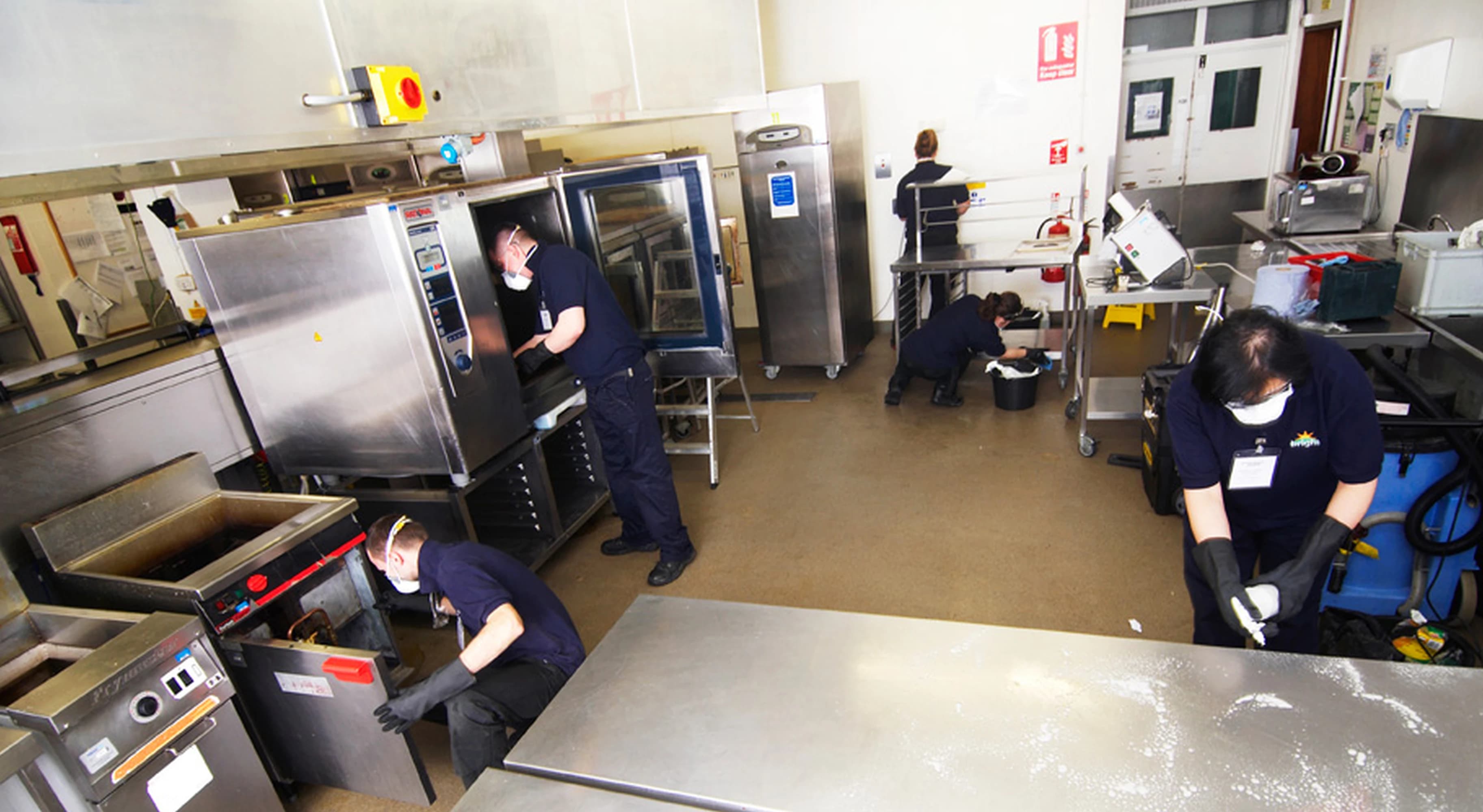 Bright cleaning team working together to maintain hygiene standards in a commercial kitchen environment.